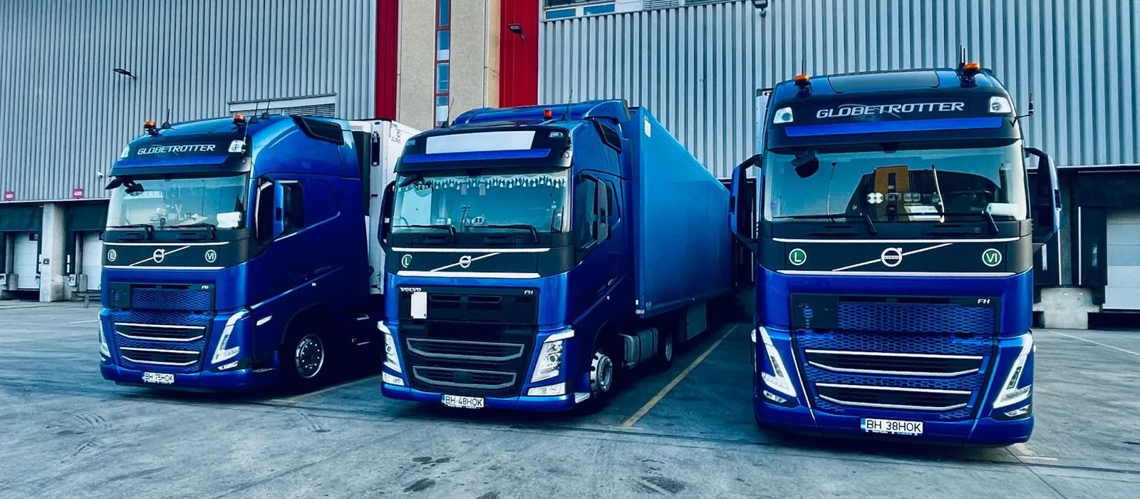 Trei camioane Volvo FH albastre Hokman Trans parcate la rampa unui depozit